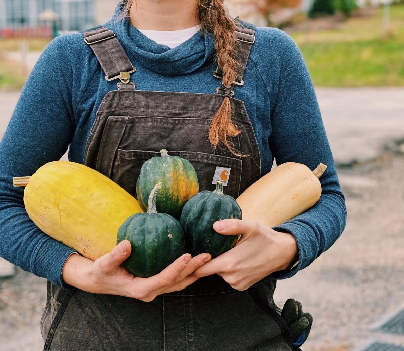 A farmer in Carhartt overalls cradling an armful of winter squash — spaghetti, acorn, and butternut
